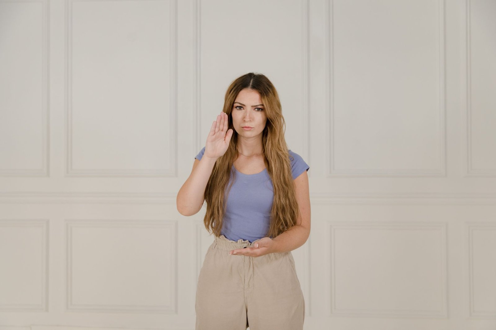 Assertiveness Skills Certification - A woman in a blue t-shirt using sign language. Neutral background enhances focus on communication.