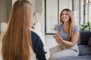 Improve Your Social Skills Certification - Smiling women having a conversation indoors, gesturing positively.