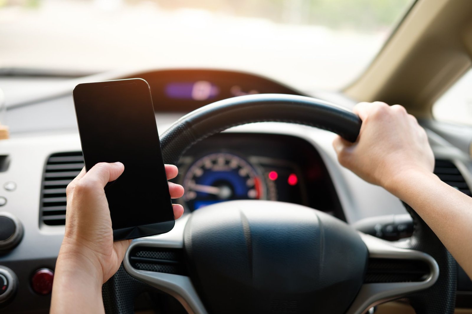 Mobile Phones and Driving Certification - A driver uses a smartphone while steering a vehicle, showcasing distracted driving risks.