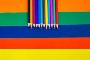 Colour Therapy Certification - A collection of colored pencils arranged on a bright striped background, showcasing vivid rainbow hues.