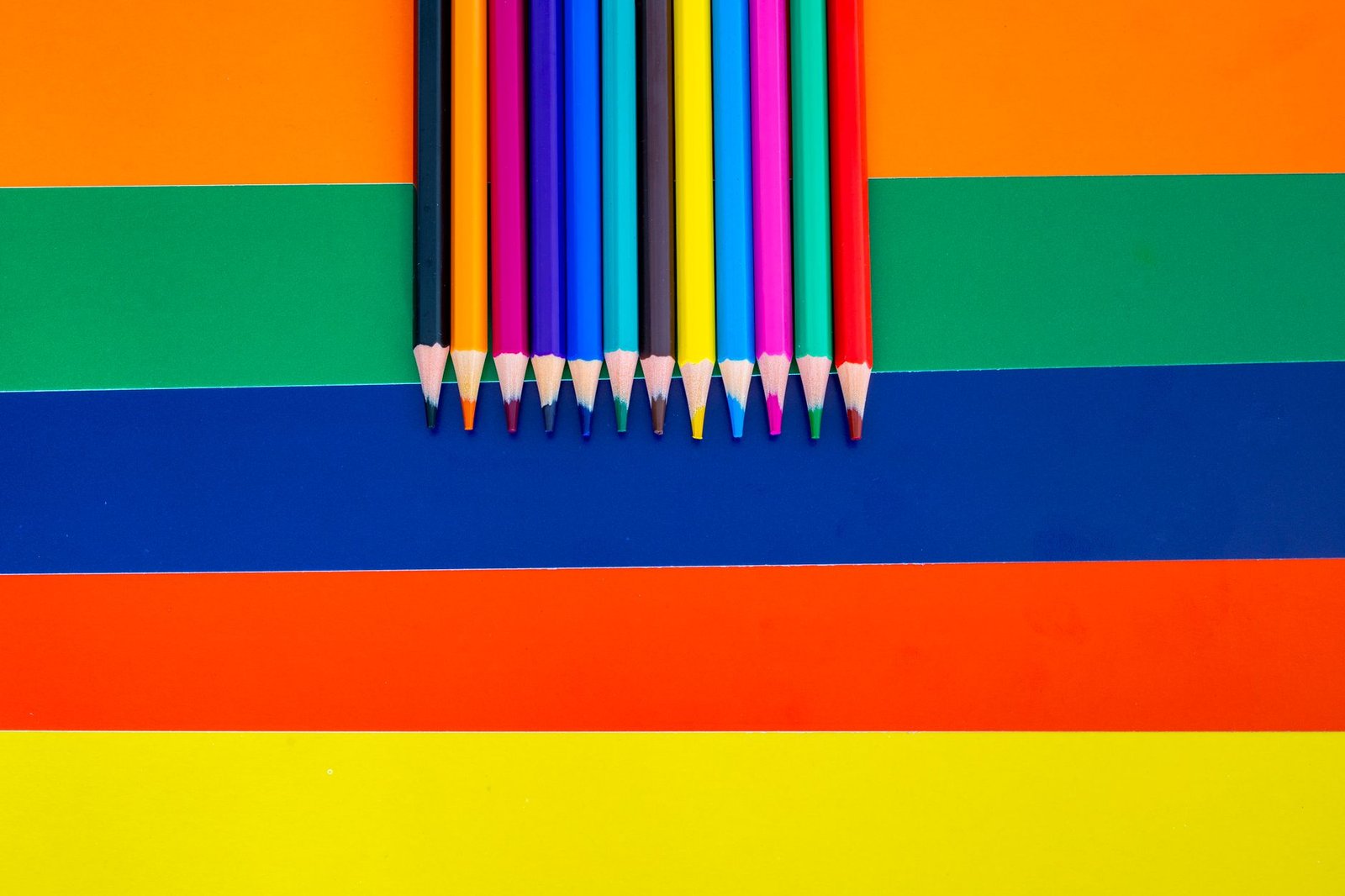 Colour Therapy Certification - A collection of colored pencils arranged on a bright striped background, showcasing vivid rainbow hues.