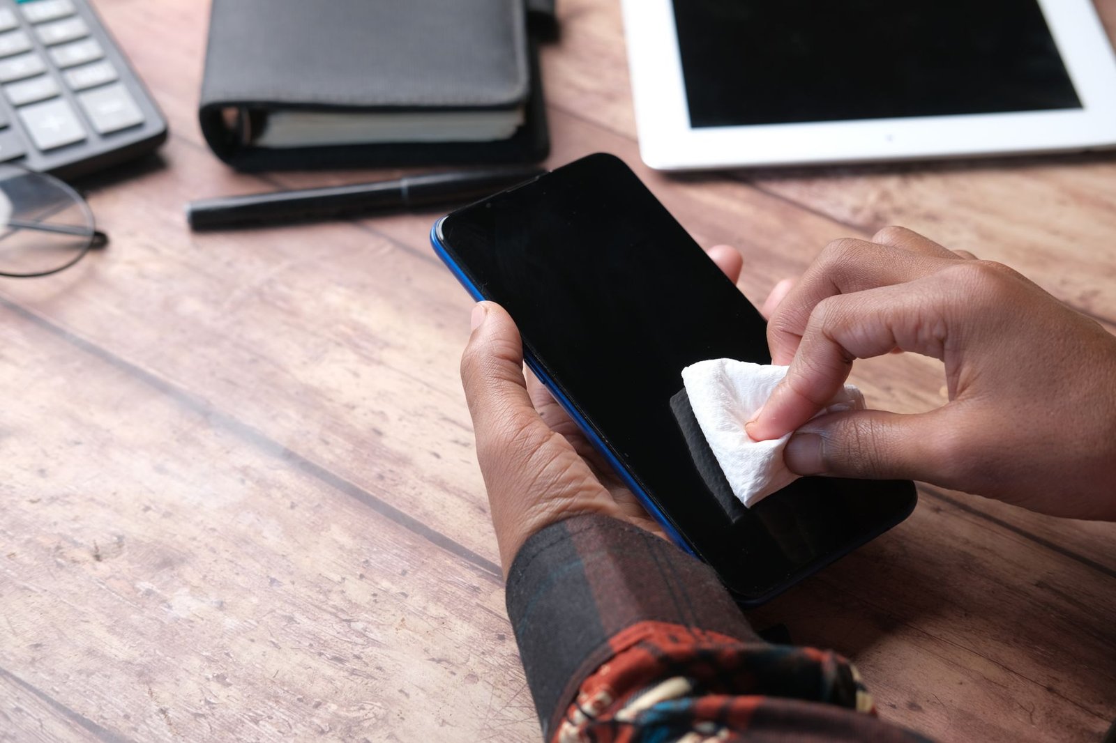 Workplace Hygiene Certification - Hands wiping a smartphone with a cloth in an organized workspace. Emphasizes hygiene and device care.