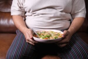Tackling Obesity Certification - Individual sitting on a couch holding a bowl of vegetable salad, showcasing a healthy lifestyle.