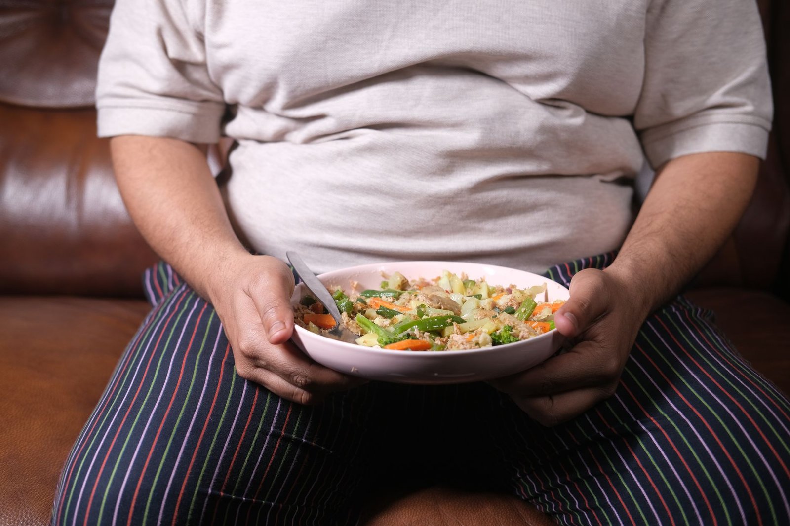 Tackling Obesity Certification - Individual sitting on a couch holding a bowl of vegetable salad, showcasing a healthy lifestyle.