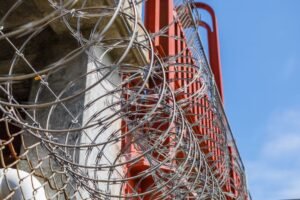 Physical Security - Close-up of barbed wire on an industrial fence against a blue sky.