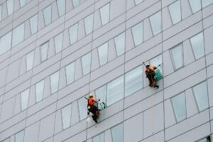 Facilities Management Certification Level 2 - High-rise window washers in safety gear cleaning a skyscraper facade.