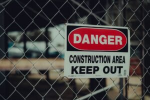 The Dangers of Construction Dust Certification - Close-up of a warning sign on a chain link fence at a construction site indicating danger.