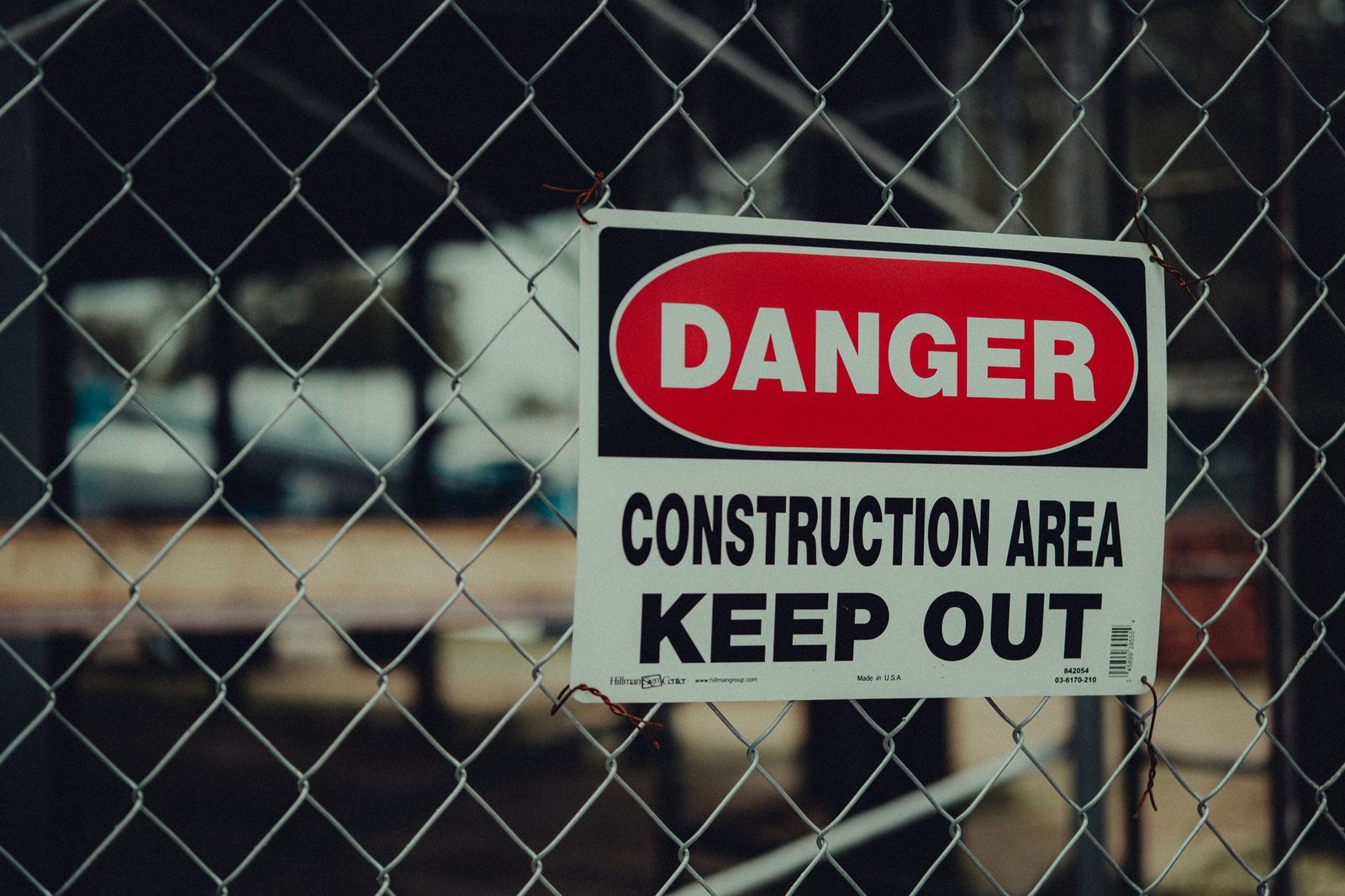 The Dangers of Construction Dust Certification - Close-up of a warning sign on a chain link fence at a construction site indicating danger.