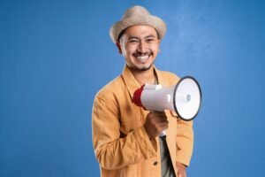 Influencing People Certification - Cheerful man holding a megaphone and wearing a hat, set against a blue background.