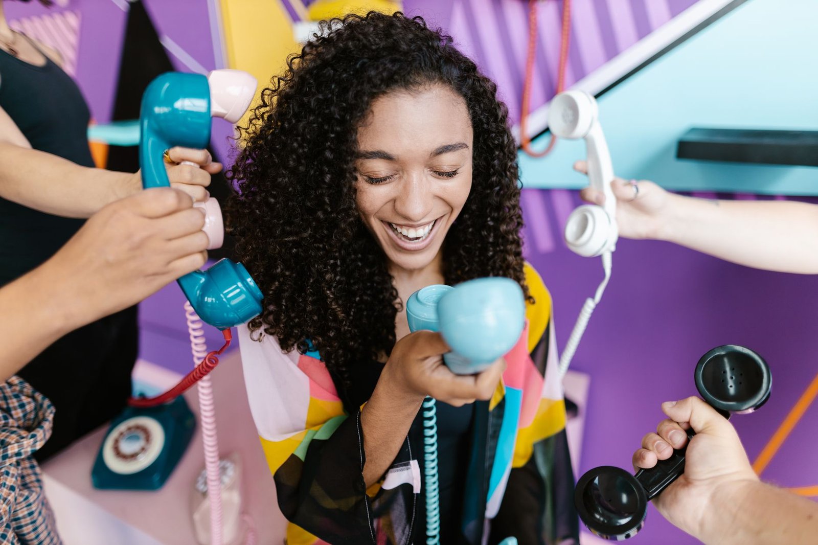 Telephone Etiquette Certification - Joyful woman with curly hair amid colorful retro telephones, showcasing vintage communication.