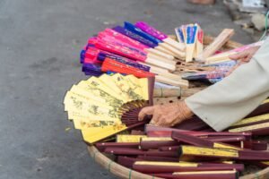 Selling Your Arts and Crafts Certification - A close-up of a vendor showcasing handmade decorative fans on a street market.
