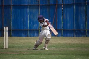 Child Protection in Sport Certification - A young cricketer in action on a sunny day, playing on a grass field with a bat and wicket.