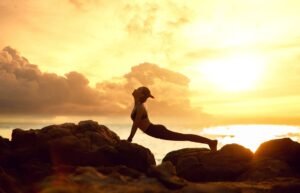 Hatha Yoga Foundation Level Certificate - Silhouette of a woman doing yoga on a rocky beach at sunset, perfect for relaxation themes.