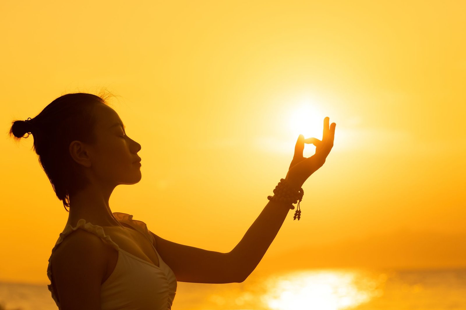 Spirituality Coach Certificate - Silhouette of a woman meditating by the sea during a vibrant sunset, creating a peaceful atmosphere.