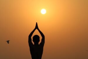 Yoga – Sun Salutations Certificate - A serene silhouette of a person meditating with hands raised towards the sunset.