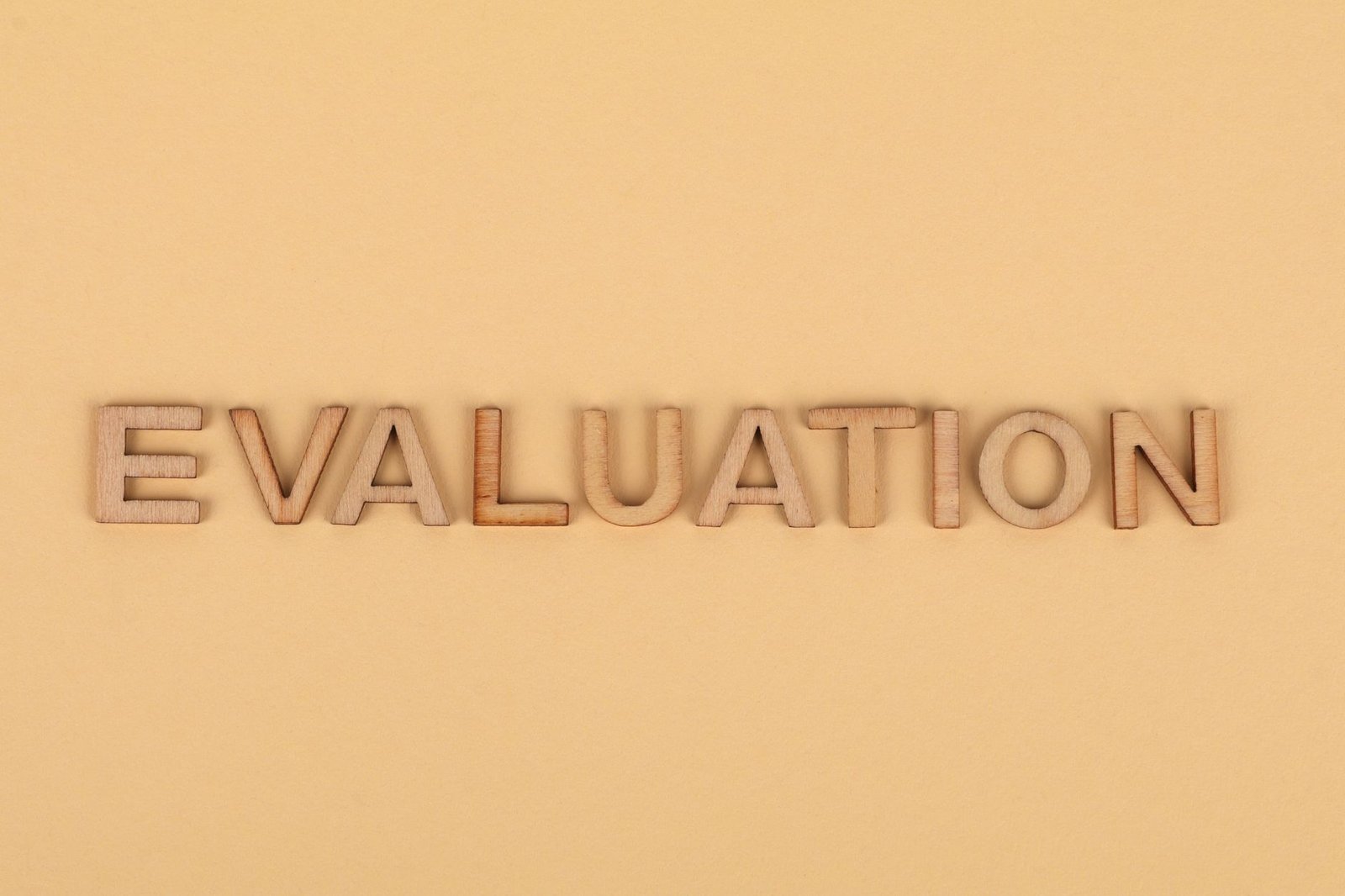 Training Delivery and Evaluation Certification - Wooden letter blocks arranged to spell 'evaluation' on a beige background.