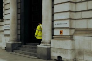 Dealing with HMRC in Relation to New Employees Certification - A guard in yellow jacket at the entrance of HM Revenue & Customs building in the UK.
