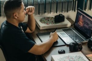 Introduction to Graphic Design Certification - A photographer working at a creative setup with a laptop and Wacom tablet, focused on editing photos indoors.