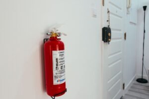 Basic Fire Safety Awareness Certification - Red fire extinguisher mounted on a white wall in a modern apartment hallway.