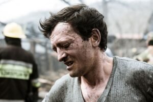 Trauma Awareness Certification - A distraught man with dirt-stained face looks distressed amidst firefighters tackling a crisis.