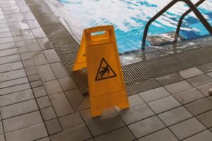 Preventing Slips and Trips in the Workplace Certification - A caution wet floor sign placed near a swimming pool to ensure safety around the slippery area.