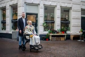 Health and Safety Basics and Essentials Certification - Elderly woman in wheelchair with companion outdoors in 's-Hertogenbosch.