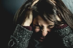 Challenging Behaviour Awareness Certification - Close-up of a woman in distress with eyes closed and hands in hair, expressing anxiety.