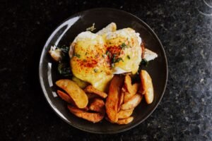 Food Allergen Awareness & Benedict’s Law Certification - Delicious Eggs Benedict with creamy sauce and crispy potato wedges served on a dark plate.
