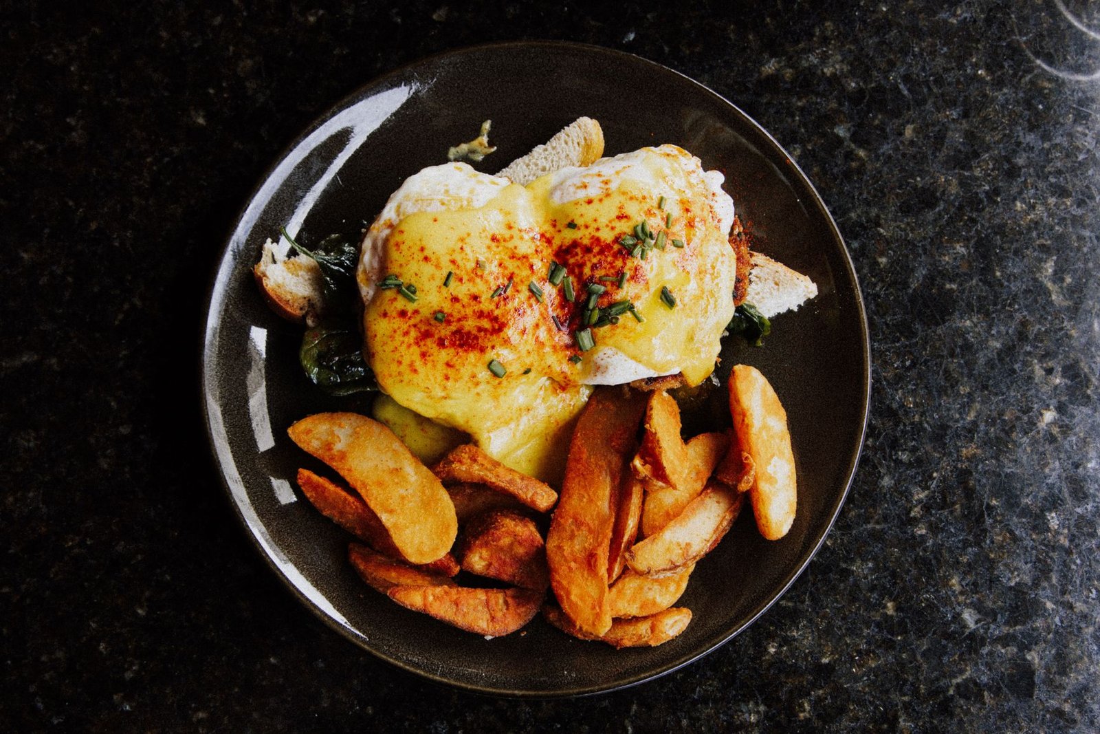 Food Allergen Awareness & Benedict’s Law Certification - Delicious Eggs Benedict with creamy sauce and crispy potato wedges served on a dark plate.