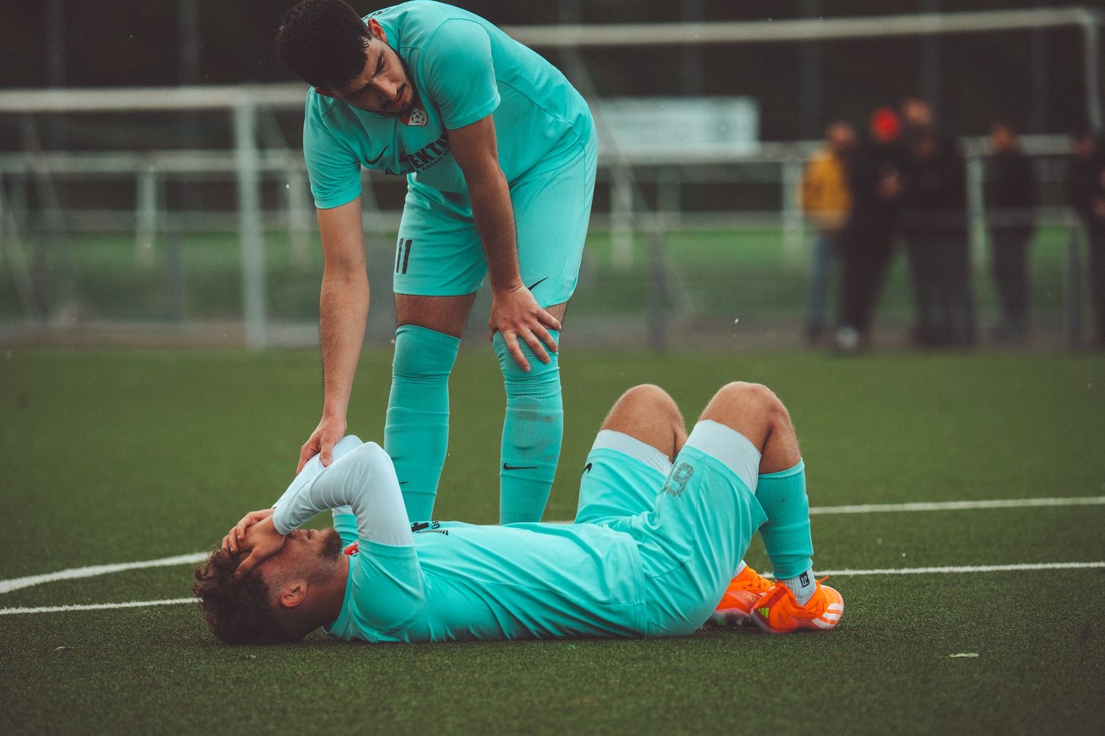 Sports Psychology Certification - A soccer player lying on the grass field being consoled by a teammate in sportswear.