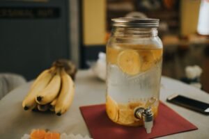 Nutrition and Hydration Certification - Citrus-infused water in a mason jar with bananas on a cozy kitchen table.