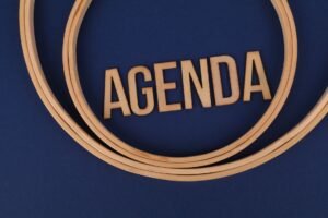 Agenda Setting Certification - Wooden letters form the word 'AGENDA' encircled by hoops on a blue surface, suggesting planning and strategy.