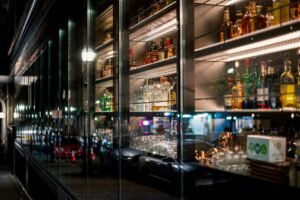 Applying for Alcohol Licensing Certification - Bar shelves with a variety of liquor bottles and reflections of street lights at night.