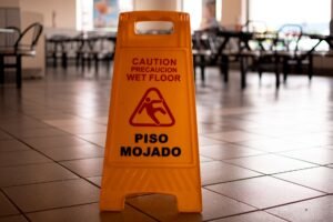 Slips, Trips and Falls Certification - Yellow caution wet floor sign in a cafeteria warns of slippery conditions on tiled floor.