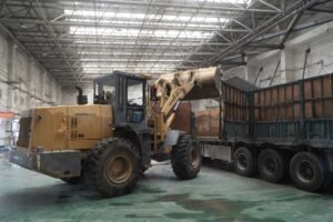 Working with Forklift Trucks Certification - Heavy-duty loader transferring materials onto a truck inside a large warehouse.