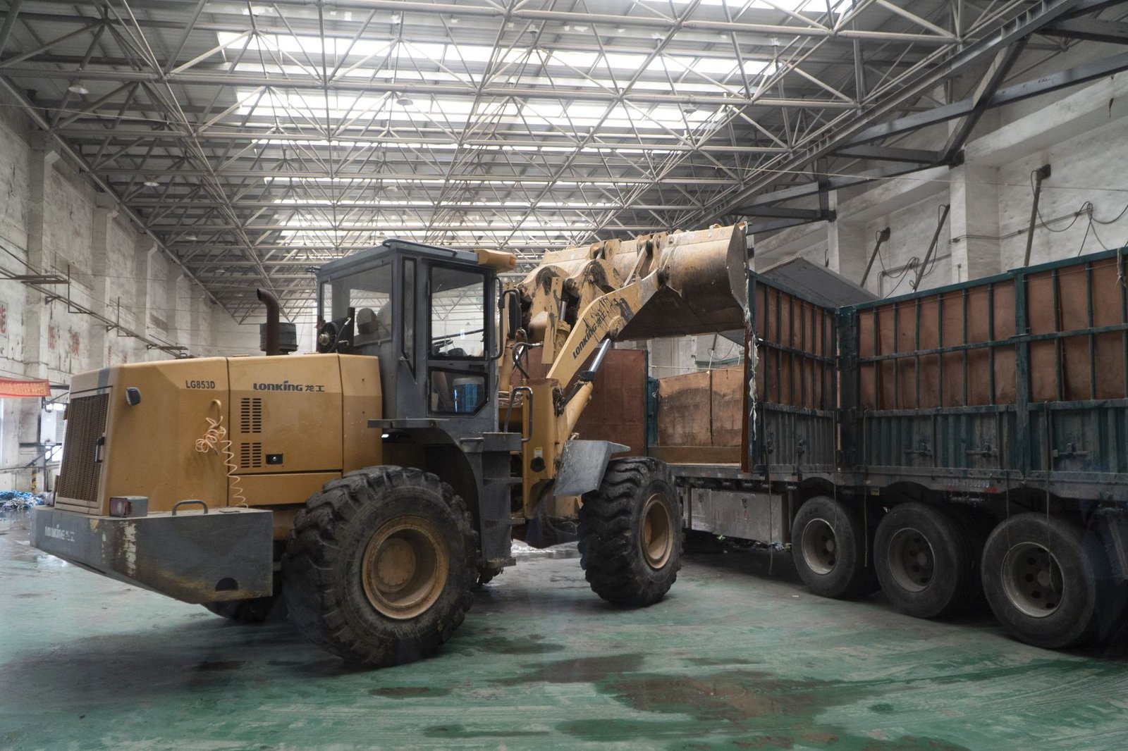 Working with Forklift Trucks Certification - Heavy-duty loader transferring materials onto a truck inside a large warehouse.