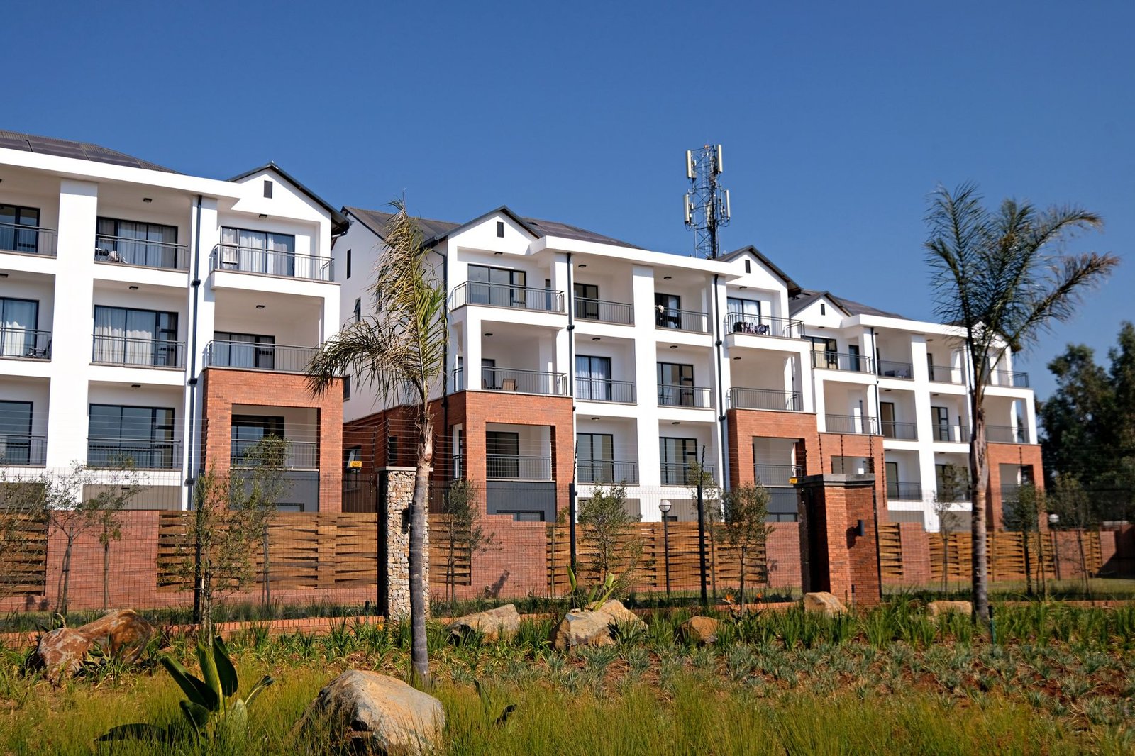 Property Development Certification - Contemporary apartment complex with garden, featuring white facade and red brick accents.