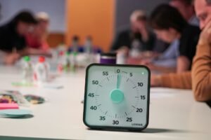 Designing Effective Teams Certification - Timer on a table with blurred people in an office meeting setting, emphasizing focus.