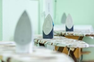 Start Your Own Ironing Business Diploma - Close-up of modern irons placed on ironing boards with camouflage pattern covers in a bright indoor setting.