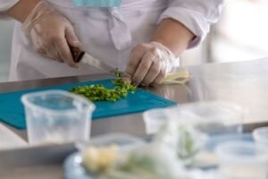 Food Safety Level 1 Certification - A chef expertly chops fresh herbs on a blue cutting board in a professional kitchen environment.
