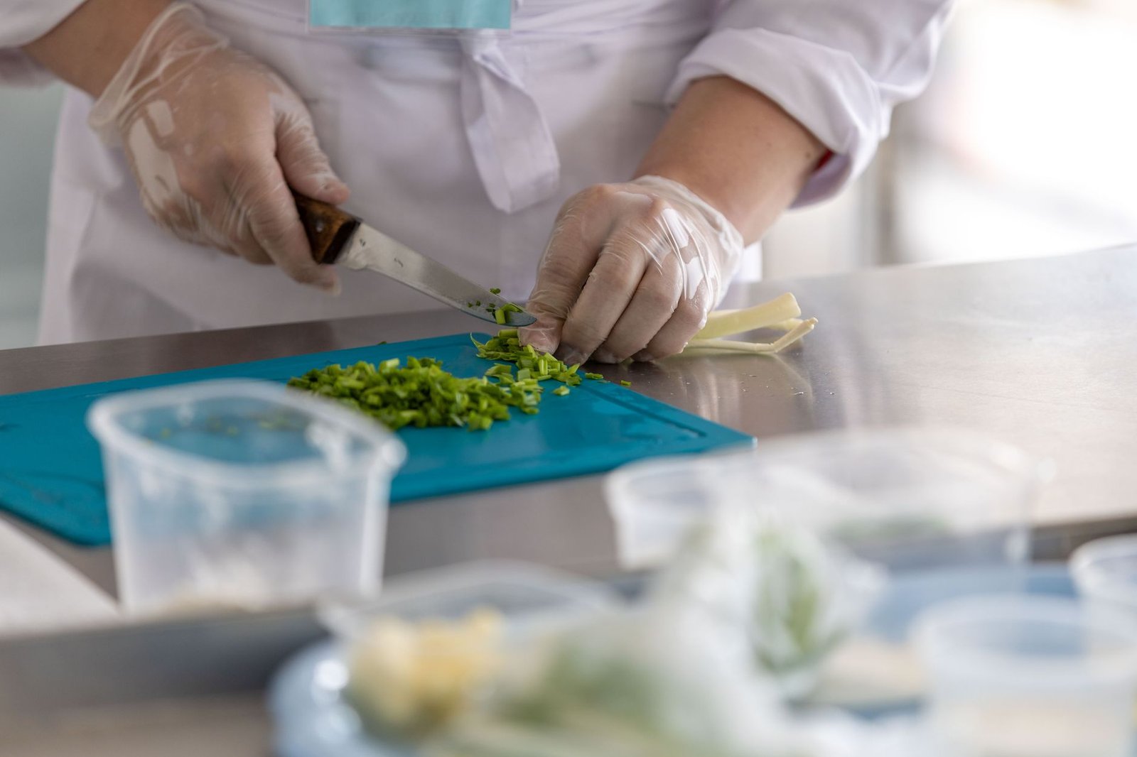 Food Safety Level 1 Certification - A chef expertly chops fresh herbs on a blue cutting board in a professional kitchen environment.