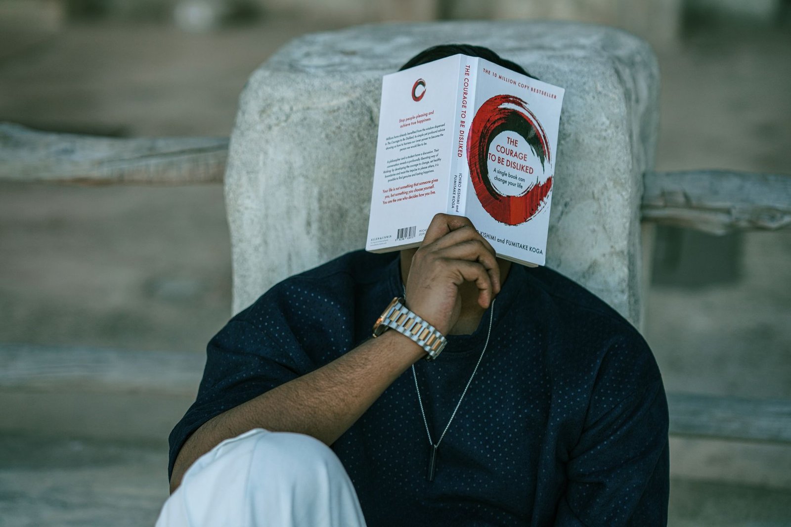 Success Habits Certification - A man reads 'The Courage to Be Disliked' in an outdoor setting, focusing on self-improvement and mindfulness.