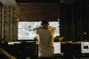 Online Security Certification - A man stands thoughtfully in a dimly lit control room with various screens.