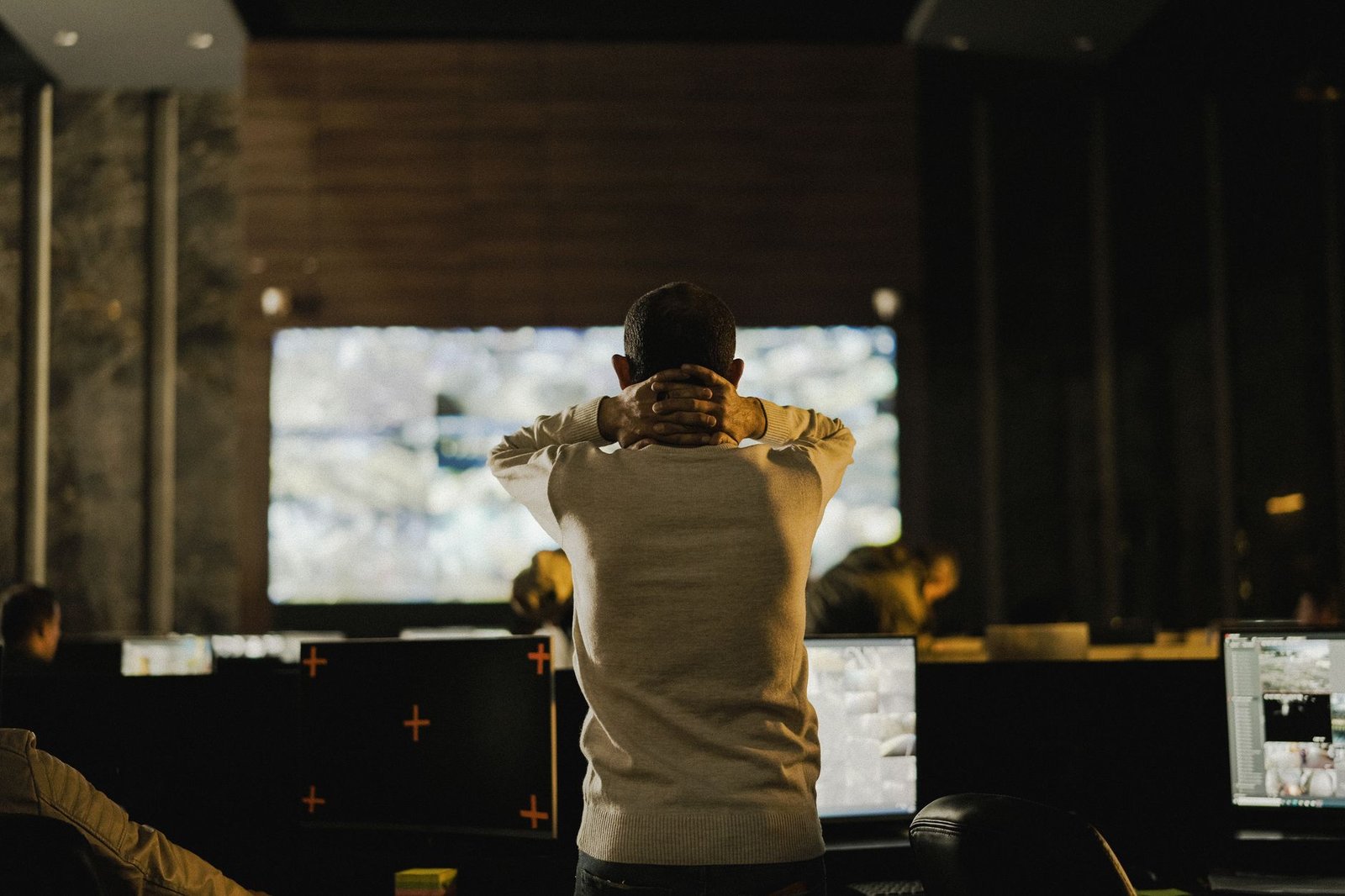 Online Security Certification - A man stands thoughtfully in a dimly lit control room with various screens.