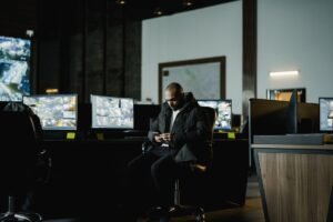 Workplace Monitoring and Data Protection Certification - Security officer seated in a dimly lit control room, analyzing multiple surveillance screens.