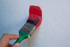 Painting and Decorating Certification - Detailed image of a hand holding a paintbrush with red paint on a textured wall.