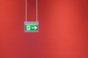 Introduction to Emergency Procedures in the Workplace Certification - Green emergency exit sign with arrow on vibrant red wall, indicating direction for safety.