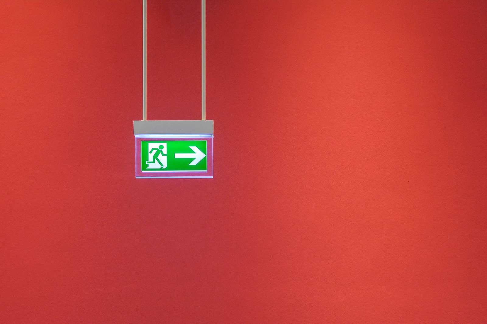 Introduction to Emergency Procedures in the Workplace Certification - Green emergency exit sign with arrow on vibrant red wall, indicating direction for safety.
