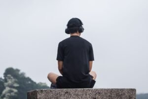 Mindful Listening Certification - A teenager sitting cross-legged outdoors, meditating with headphones for relaxation.