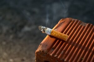 How to Stop Smoking Certification - Close-up of a smoked cigarette butt resting on a textured clay surface in outdoor light.